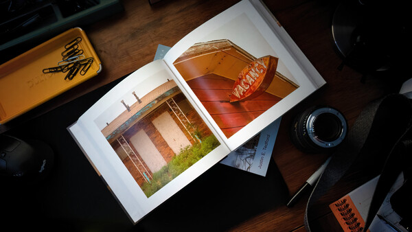 Open portfolio displaying architectural photography prints on a wooden desk with camera equipment nearby.