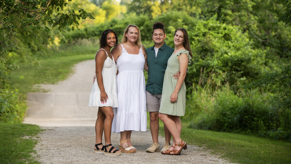 Four people standing together on a tree-lined dirt path in natural daylight.