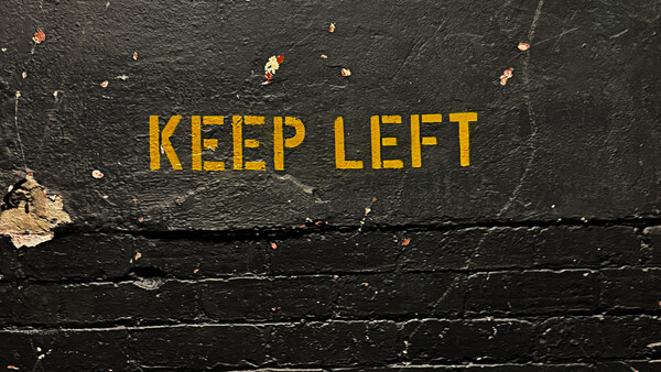 Yellow "KEEP LEFT" text painted on weathered black asphalt surface.