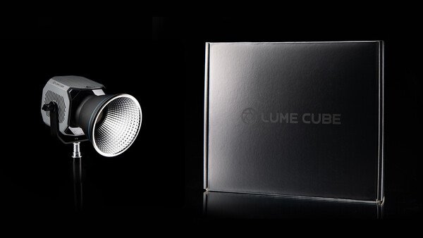 LED studio light with reflector head next to a rectangular branded box on black background.