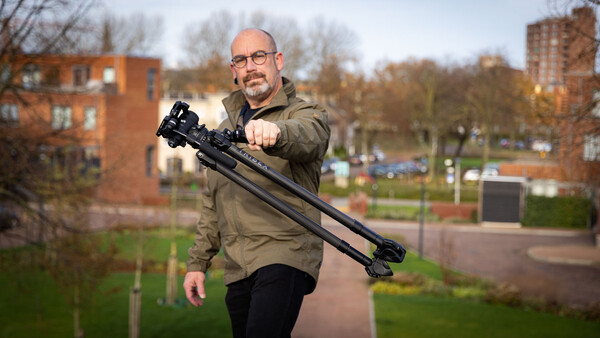 Man holding a camera stabilizer rig with mounted camera and lens in an urban park setting.
