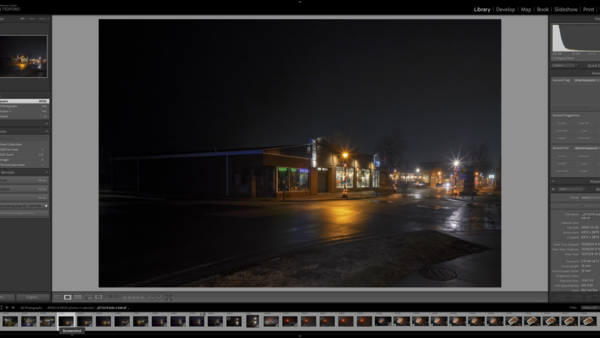 Night photograph of an illuminated commercial building with warm lighting reflected on wet pavement.