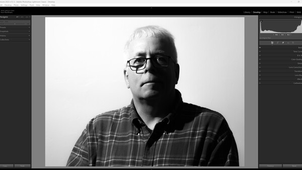 Black and white portrait of a man wearing glasses and a plaid shirt against a plain background.