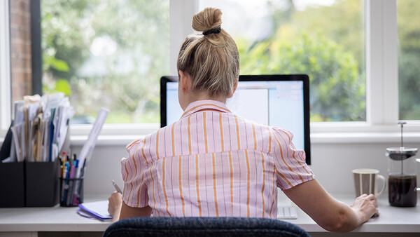 Person working at desk facing computer monitor with natural window light streaming in.