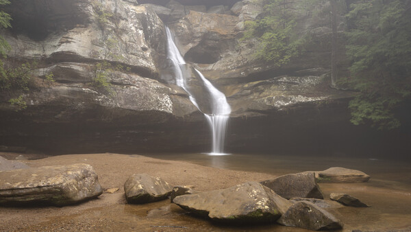 Waterfall cascading into a pool surrounded by layered rock formations and boulders.
