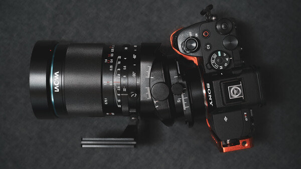 Mirrorless camera with macro lens and extension tubes arranged on dark surface.