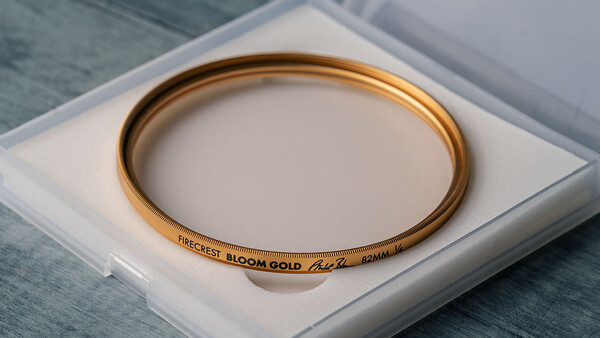 Gold-toned optical filter with engraved text displayed in white presentation box on textured surface.