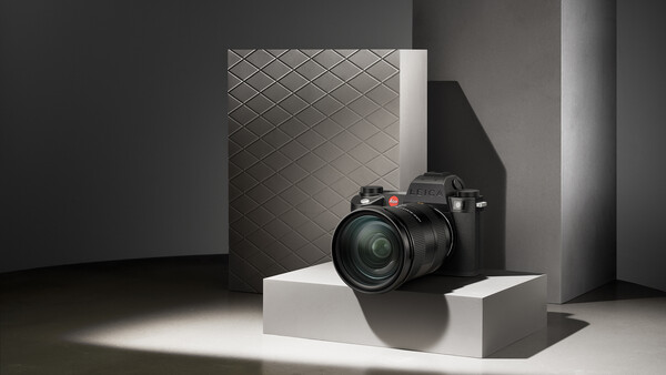 Professional mirrorless camera with telephoto lens displayed on white pedestal in minimalist studio setting.