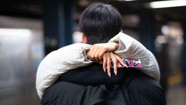 Person wearing cream-colored puffer jacket and dark clothing, photographed from behind with arm raised to shoulder.