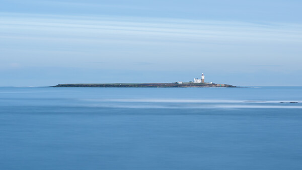 Small lighthouse on a rocky island beneath a clear blue sky and calm sea.