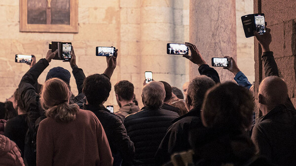 Crowd of people holding up smartphones to photograph a building facade.