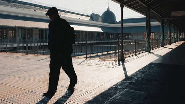 Silhouetted figure walking on a sunny rooftop terrace with architectural elements in background.