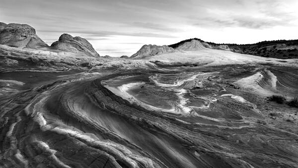 Sweeping curves of light and shadow flow across a vast volcanic landscape with distant mountains under stormy skies.