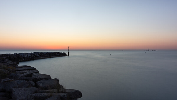 Rocky jetty extending into calm water at twilight with a solitary navigation marker visible in the distance.