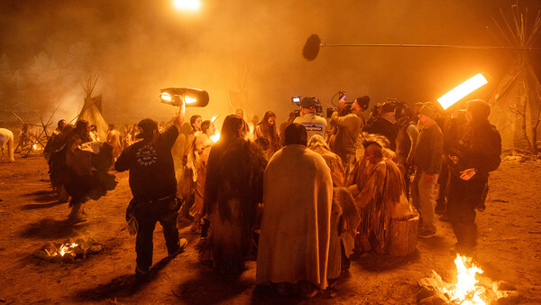 Crowd gathered around fires at night in desert setting with warm orange lighting and smoke.