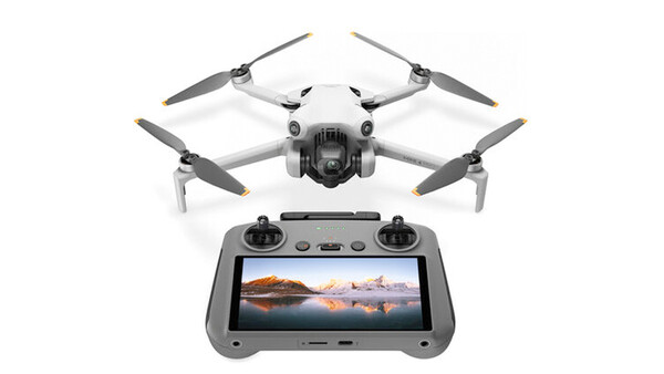 Compact drone with four propellers positioned above its remote controller displaying a landscape photograph on screen.