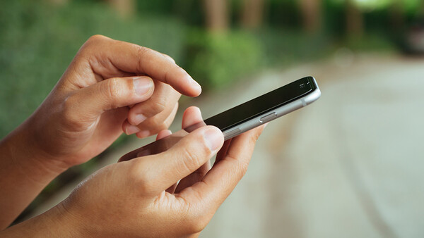 Hands holding a smartphone outdoors with natural daylight illumination.