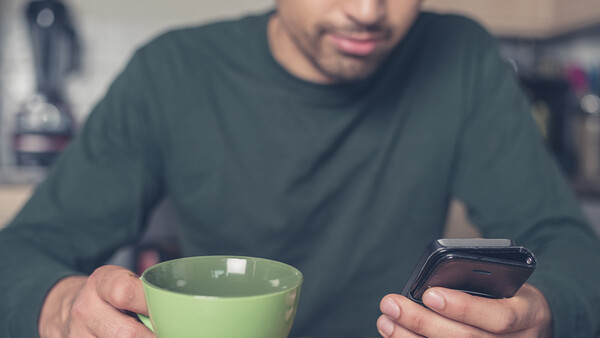 Man holding green cup and smartphone while looking at phone screen.