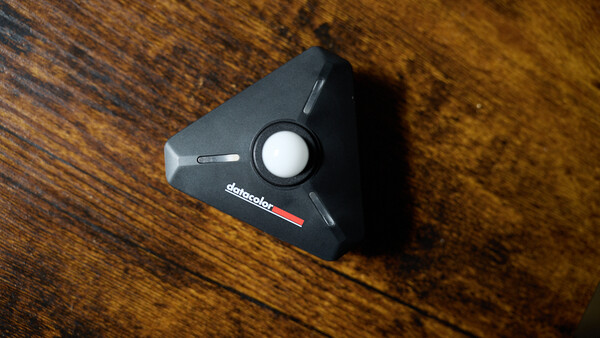 Black triangular camera accessory with white circular button on wooden surface.