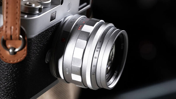 Vintage rangefinder camera with chrome lens and leather strap, shot against dark background.
