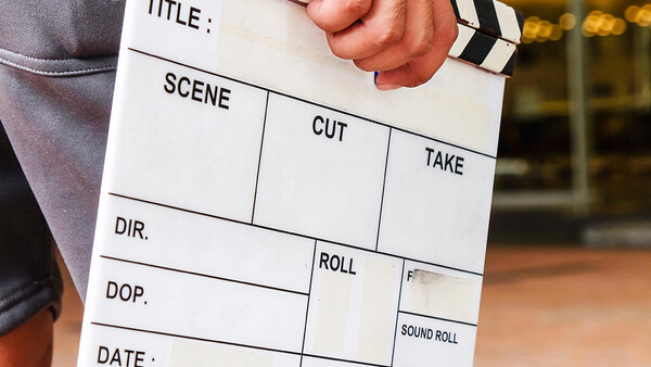 Film production clapperboard held in someone's hands, showing blank fields for title, scene, cut, take, director, and other production details.