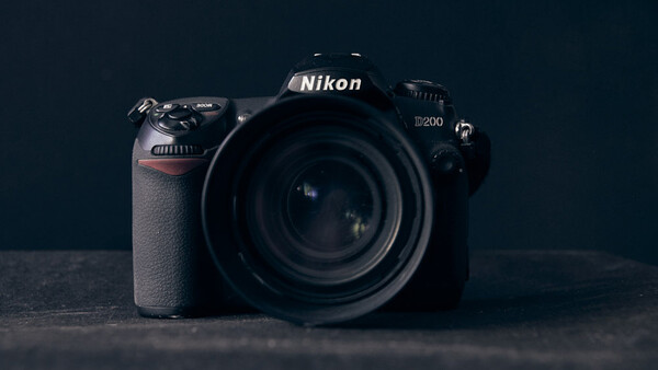 Nikon D200 DSLR camera with attached lens, positioned against a dark background.