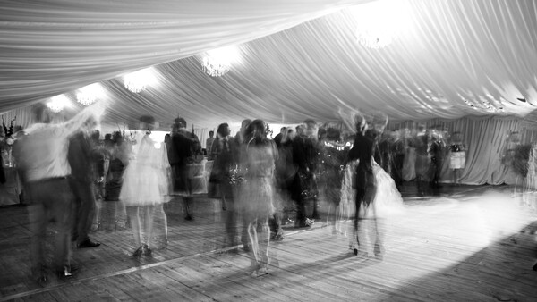 Black and white photograph of guests mingling under a draped tent at an indoor event.