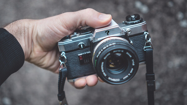 Hand holding a vintage rangefinder camera with leather body and attached neck strap.