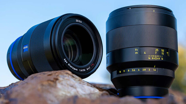 Two Zeiss camera lenses positioned on a textured rock surface against a blue sky.