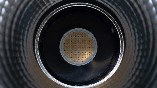 Looking directly into a cylindrical metal duct with concentric ridged walls and a perforated metal grate at the center.