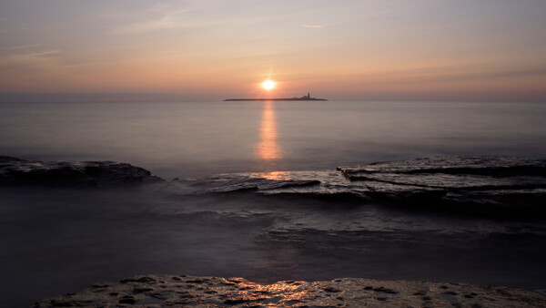 Sun setting over the ocean with a distant island silhouette and golden light reflecting on calm waves.