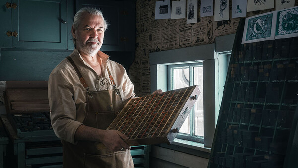 Craftsman holding a wooden sample board with diagonal wood grain pattern in his workshop.