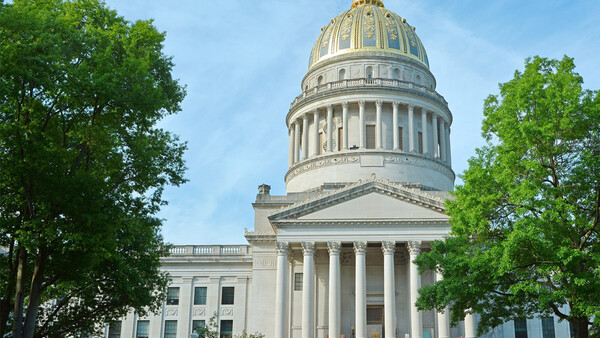 Classical government building with white columns and gold dome framed by green trees.
