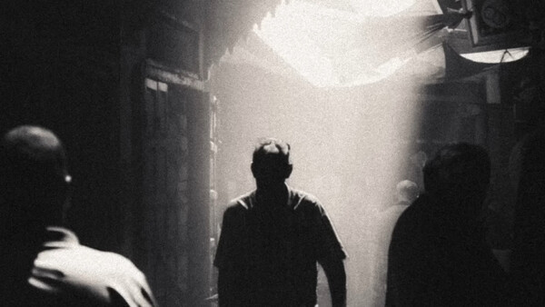 Silhouetted figures in a narrow alleyway with dramatic overhead lighting creating atmospheric shadows.
