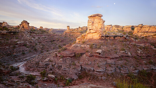 Golden-hour sunlight illuminates layered sandstone formations and rock outcroppings in an arid canyon landscape.