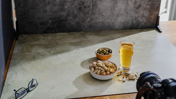 Styled flat lay with nuts, olives, juice, and eyeglasses on a concrete surface.