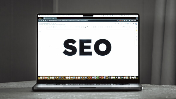 Laptop screen displaying the word 'SEO' in large black text on a white background.