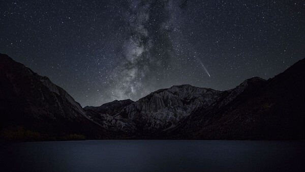 Milky Way galaxy arches over a dark mountain landscape reflected in still water below.