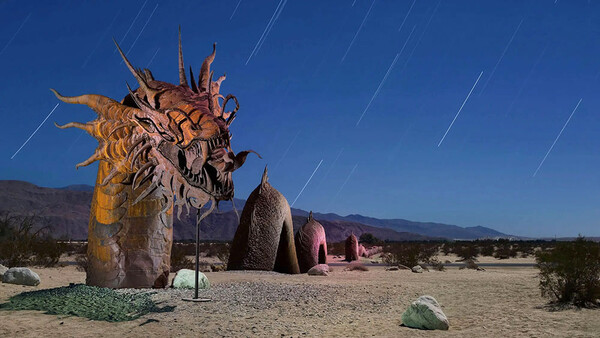 Large wooden sculpture of a stylized head with prominent features in a desert landscape at dusk.