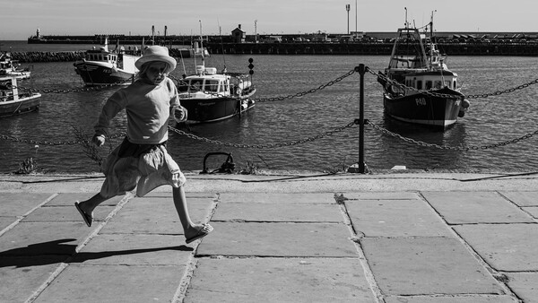 Runner in motion on a waterfront promenade with moored boats in the background.