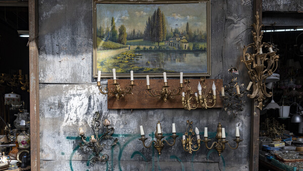 Weathered wall display with landscape painting, brass candelabras, and decorative sconces in vintage setting.