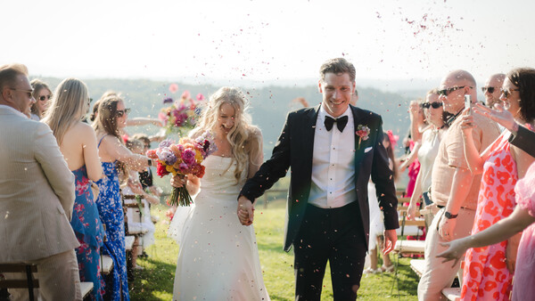 Newlyweds walk through a cheering crowd during outdoor ceremony recessional.