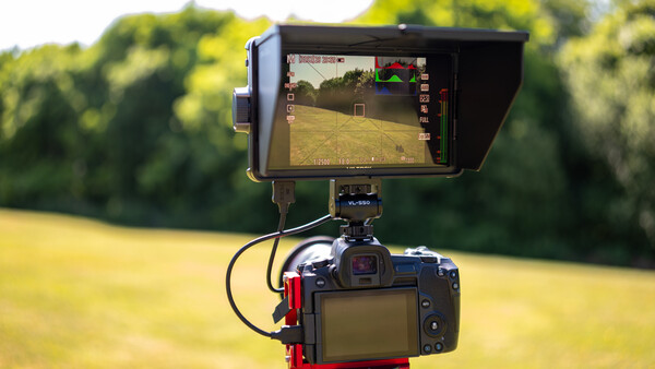 External monitor mounted on DSLR camera showing live video feed with exposure information overlay and histogram display.