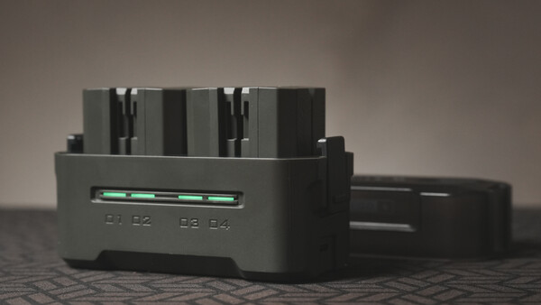 Black battery charger with four AA or AAA slots and a green LED indicator light on the front panel.