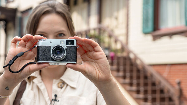 Woman holding a rangefinder film camera up to her face, positioned to take a photograph.