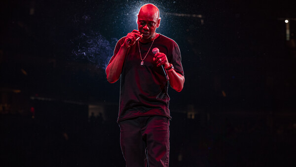 Performer on stage bathed in red lighting, holding a microphone with both hands.