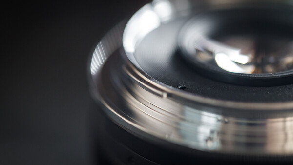 Close-up of a camera lens with selective focus, showing metal barrel and glass elements with shallow depth of field.