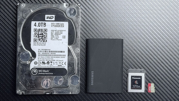 WD Black 4TB hard drive with external SSD, memory card, and microSD card on carbon fiber surface.