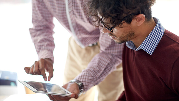 Two people examining a tablet together in an office setting with natural lighting.