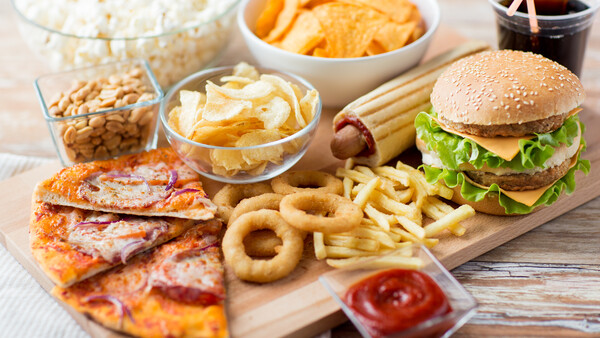 Assorted fast food and snacks arranged on a wooden board and in white bowls.